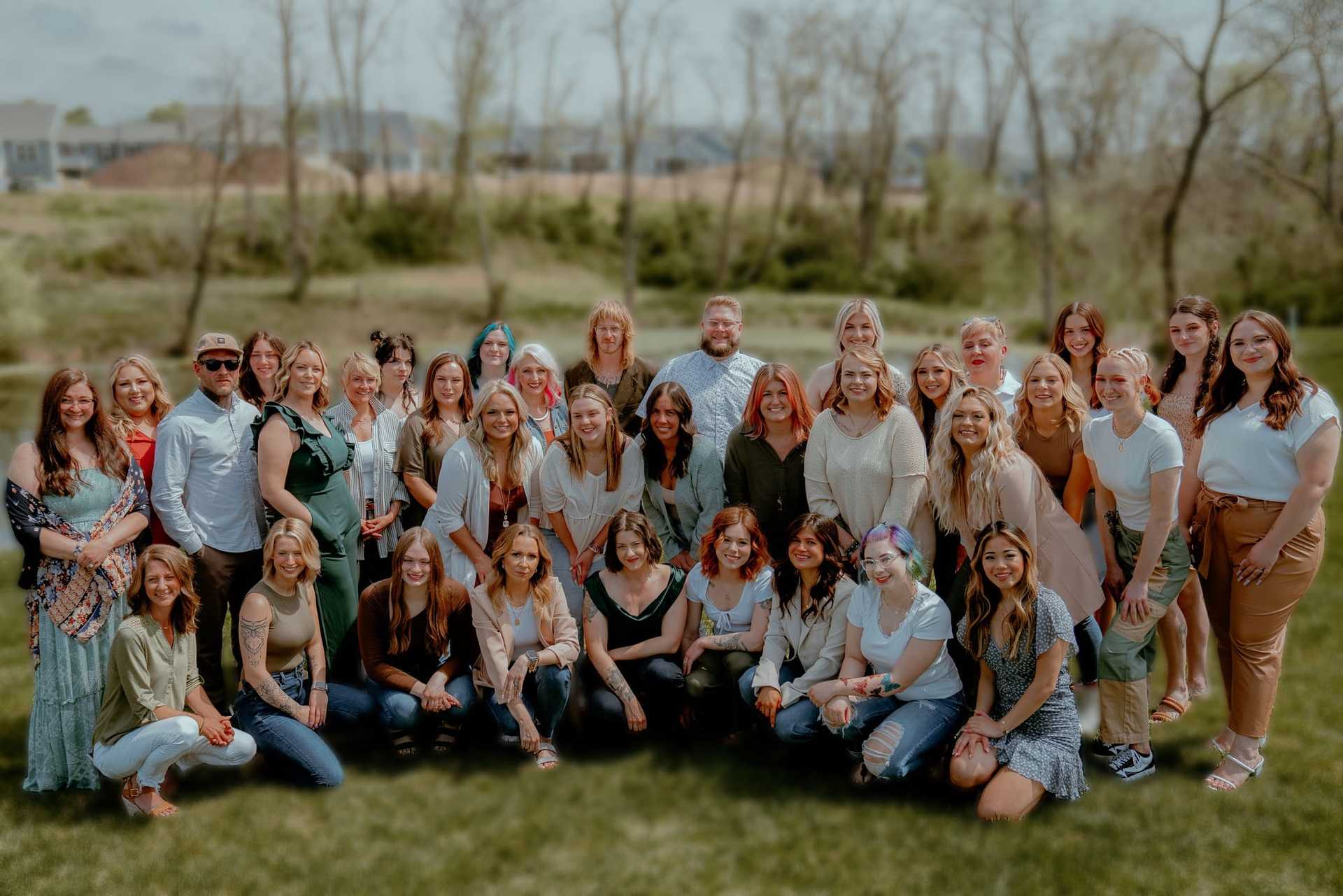 Group of people posing for a photo outdoors on a grassy area with trees in the background.