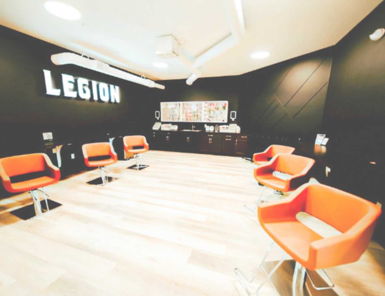 Modern salon interior with bright orange chairs and signage reading "LEGION" on the wall.