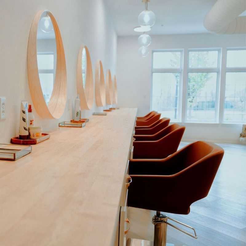 Modern salon with stylish brown chairs, circular mirrors, and large windows providing natural light.