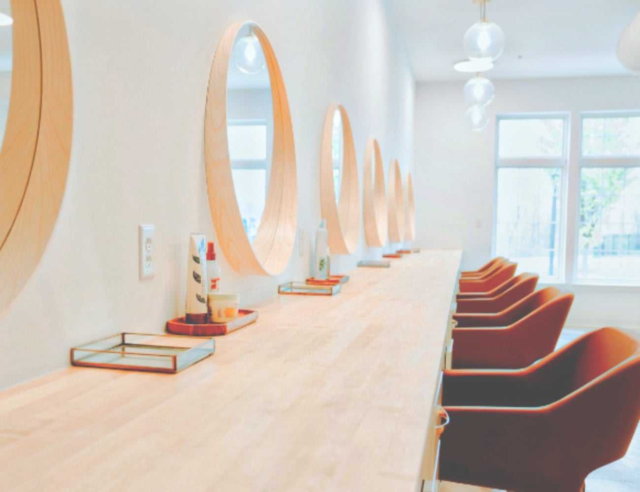 Modern salon interior with round mirrors and wooden furnishings.