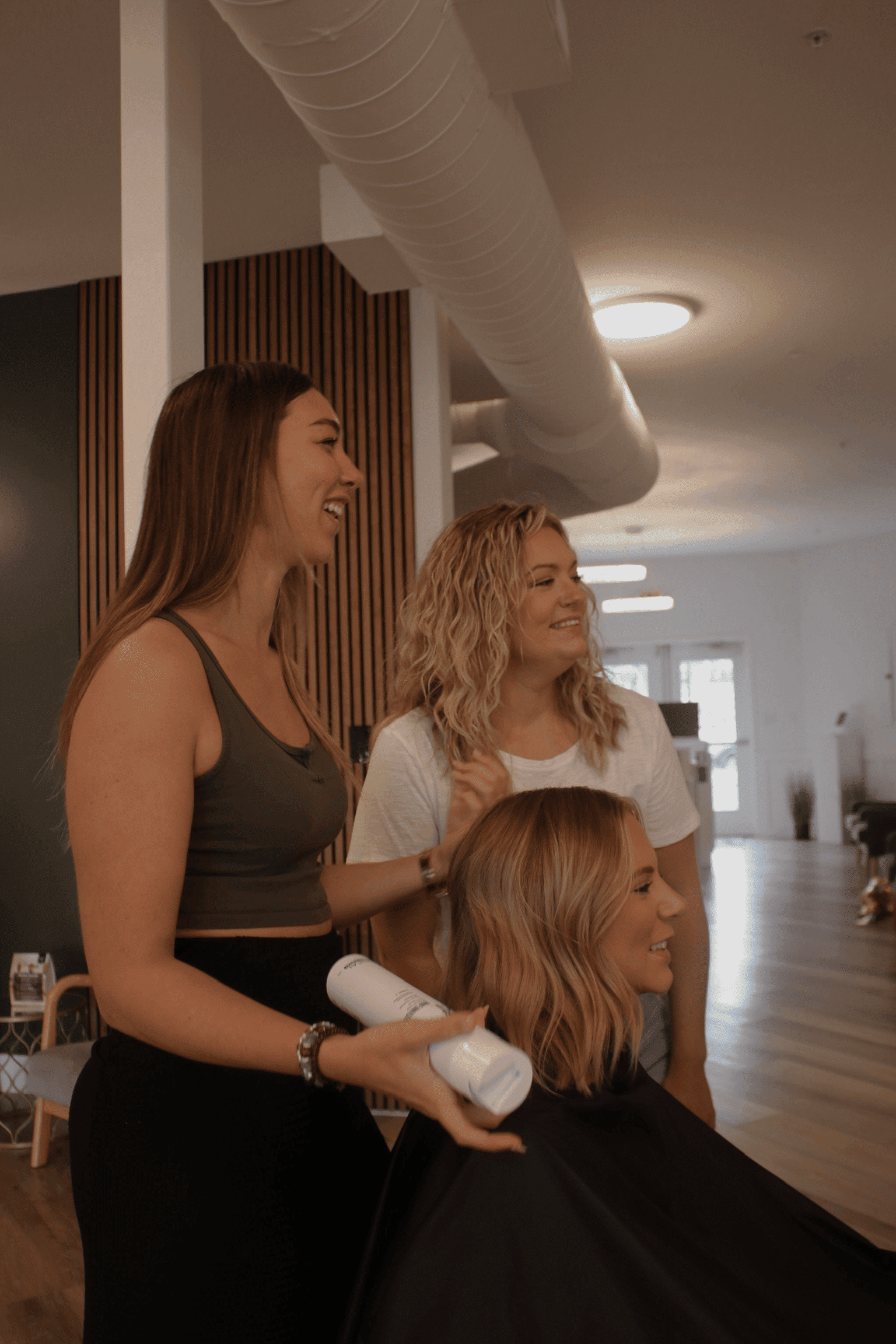 Women smiling and styling hair in a modern salon.