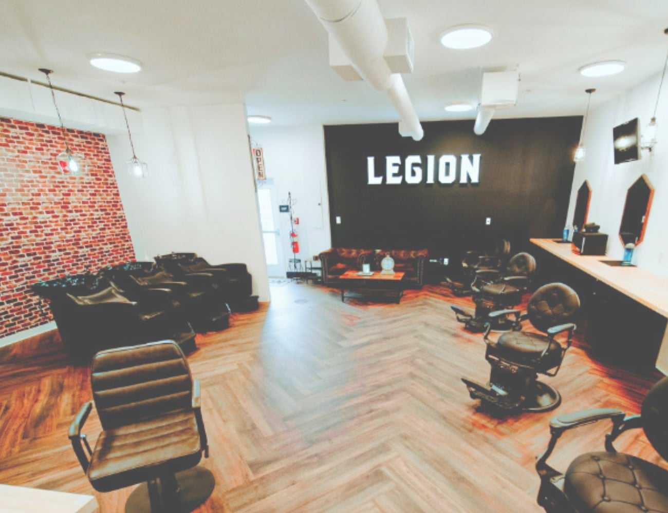 Barbershop interior with stylish chairs, brick wall, and "Legion" sign on black wall.
